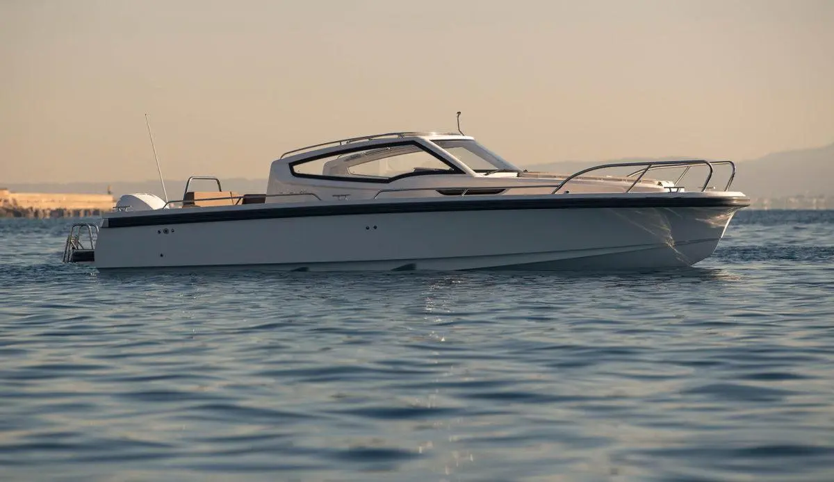 A sleek white motorboat is anchored on calm waters, reflecting the warm sunlight with a coastal background.